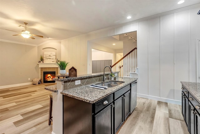 kitchen with a center island with sink, dishwasher, light wood-type flooring, a fireplace, and a sink