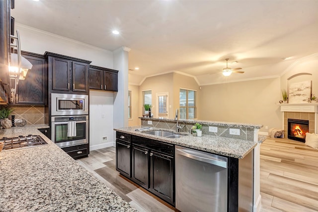 kitchen featuring tasteful backsplash, a tiled fireplace, light stone counters, stainless steel appliances, and a sink