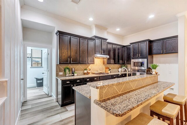 kitchen featuring a kitchen island with sink, a breakfast bar, appliances with stainless steel finishes, backsplash, and light stone countertops