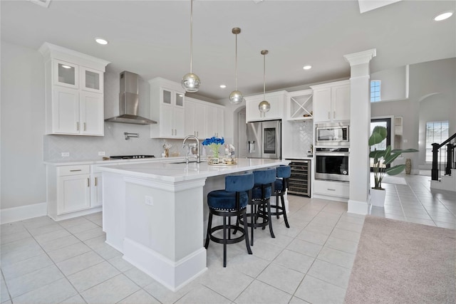 kitchen with white cabinets, wall chimney exhaust hood, hanging light fixtures, and appliances with stainless steel finishes