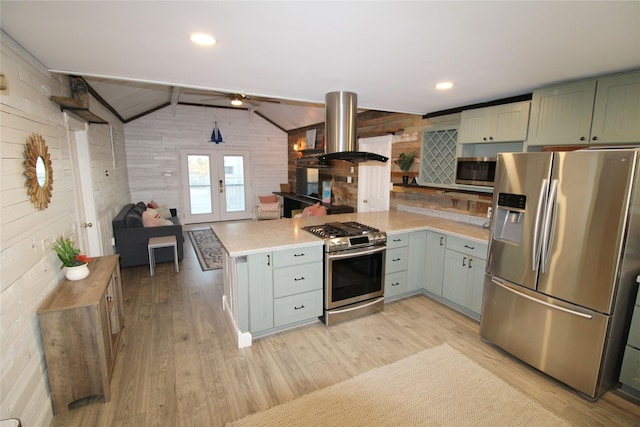 kitchen featuring kitchen peninsula, appliances with stainless steel finishes, island range hood, vaulted ceiling, and wooden walls