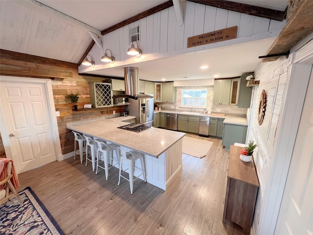 kitchen featuring pendant lighting, wooden walls, vaulted ceiling with beams, a kitchen bar, and stainless steel appliances