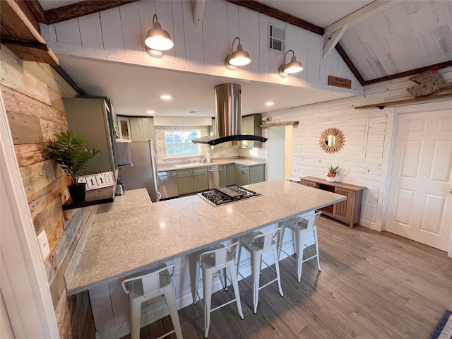 kitchen with hanging light fixtures, stainless steel appliances, kitchen peninsula, wood walls, and island range hood