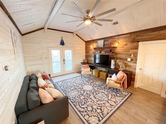 living room with french doors, wooden walls, vaulted ceiling with beams, ceiling fan, and light hardwood / wood-style floors