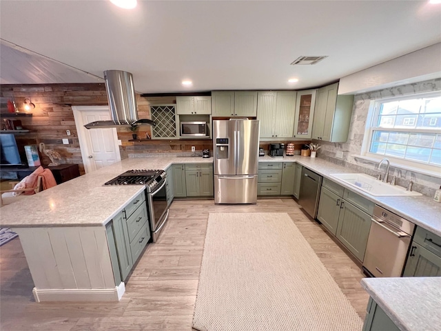 kitchen featuring appliances with stainless steel finishes, light wood-type flooring, island range hood, sink, and green cabinets