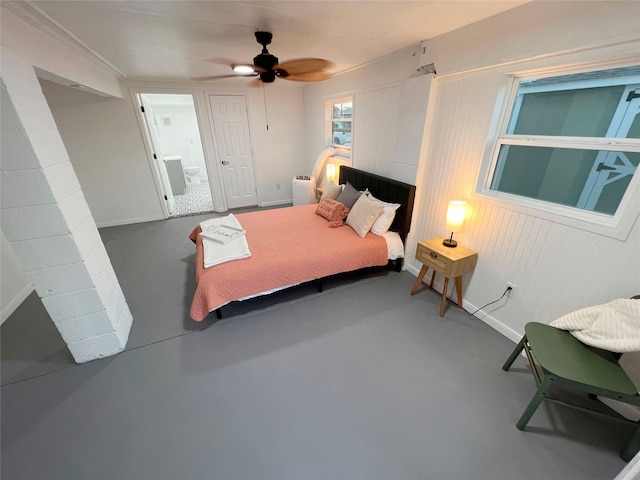 bedroom featuring concrete flooring, ensuite bath, ceiling fan, and wood walls