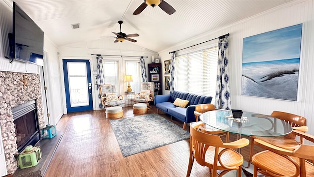 living room featuring ceiling fan, a stone fireplace, dark hardwood / wood-style flooring, lofted ceiling, and ornamental molding