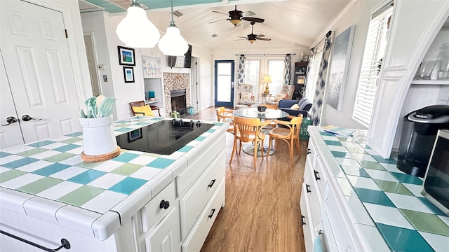 kitchen featuring white cabinets, tile countertops, vaulted ceiling, and hanging light fixtures