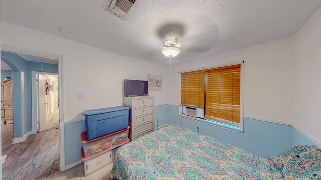 bedroom with ceiling fan, hardwood / wood-style floors, cooling unit, and a textured ceiling