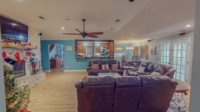 living room with french doors, crown molding, a fireplace, ceiling fan with notable chandelier, and light wood-type flooring