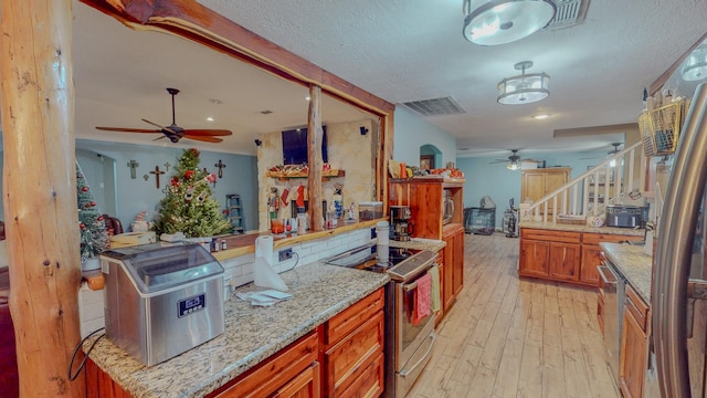 kitchen with appliances with stainless steel finishes, a textured ceiling, light hardwood / wood-style flooring, and light stone counters