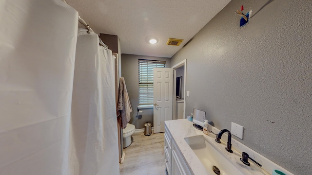 bathroom with hardwood / wood-style floors, vanity, a textured ceiling, and toilet