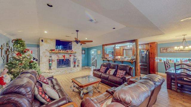 living room featuring ceiling fan with notable chandelier, light hardwood / wood-style floors, a stone fireplace, and crown molding