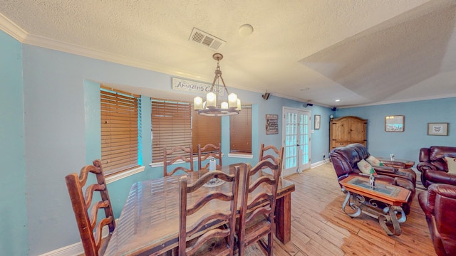 dining space featuring a notable chandelier, crown molding, light wood-type flooring, and a textured ceiling