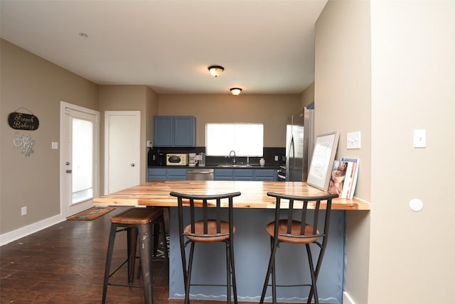 kitchen with wood counters, blue cabinets, sink, dark hardwood / wood-style flooring, and stainless steel appliances