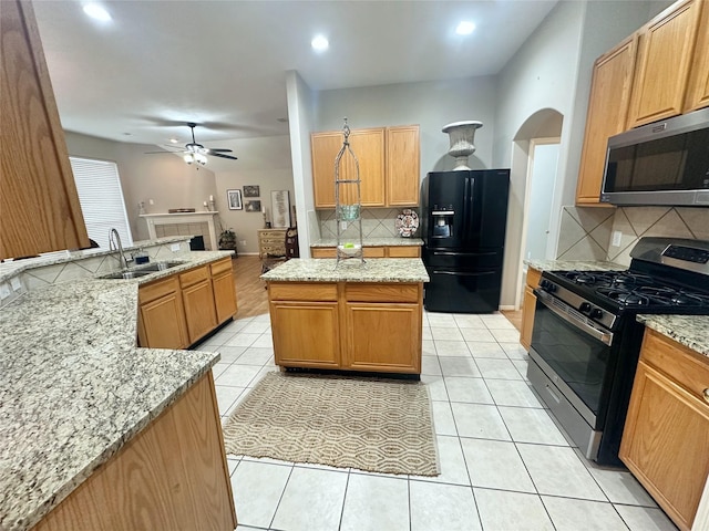 kitchen with light stone countertops, stainless steel appliances, sink, light tile patterned floors, and a kitchen island