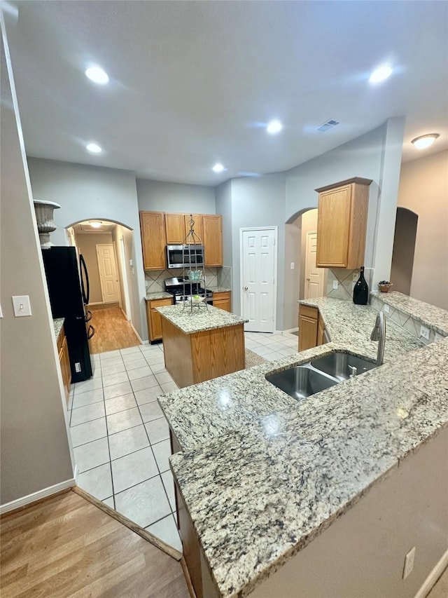 kitchen featuring kitchen peninsula, appliances with stainless steel finishes, decorative backsplash, light stone counters, and a kitchen island