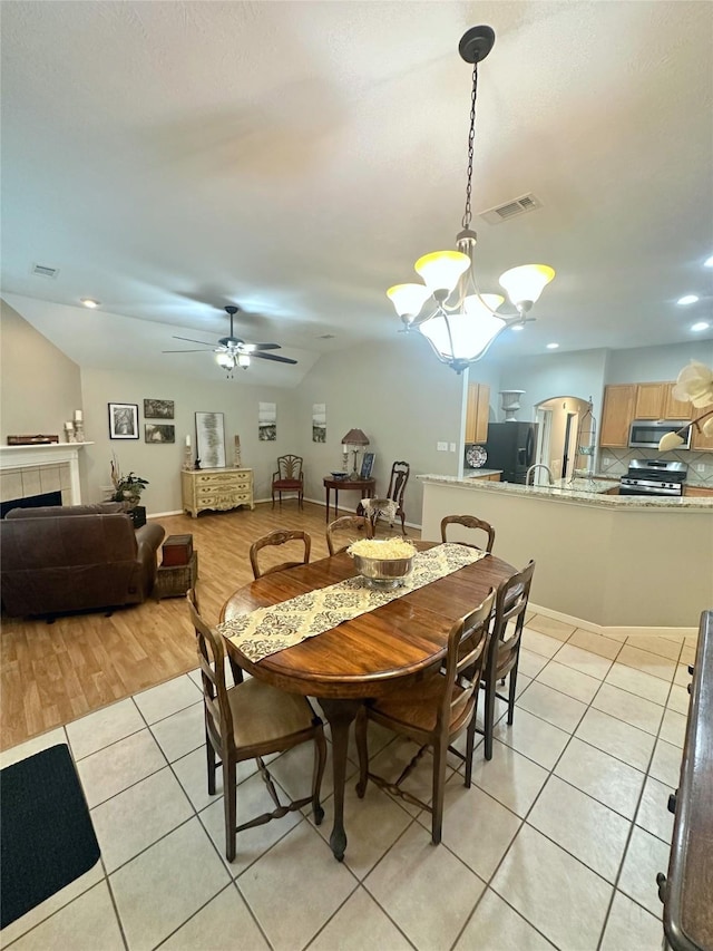 tiled dining space with ceiling fan with notable chandelier and a fireplace