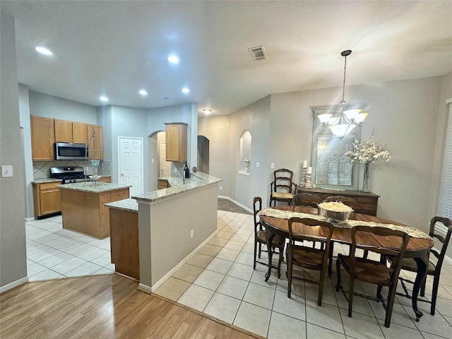 kitchen featuring hanging light fixtures, kitchen peninsula, a chandelier, light tile patterned floors, and appliances with stainless steel finishes