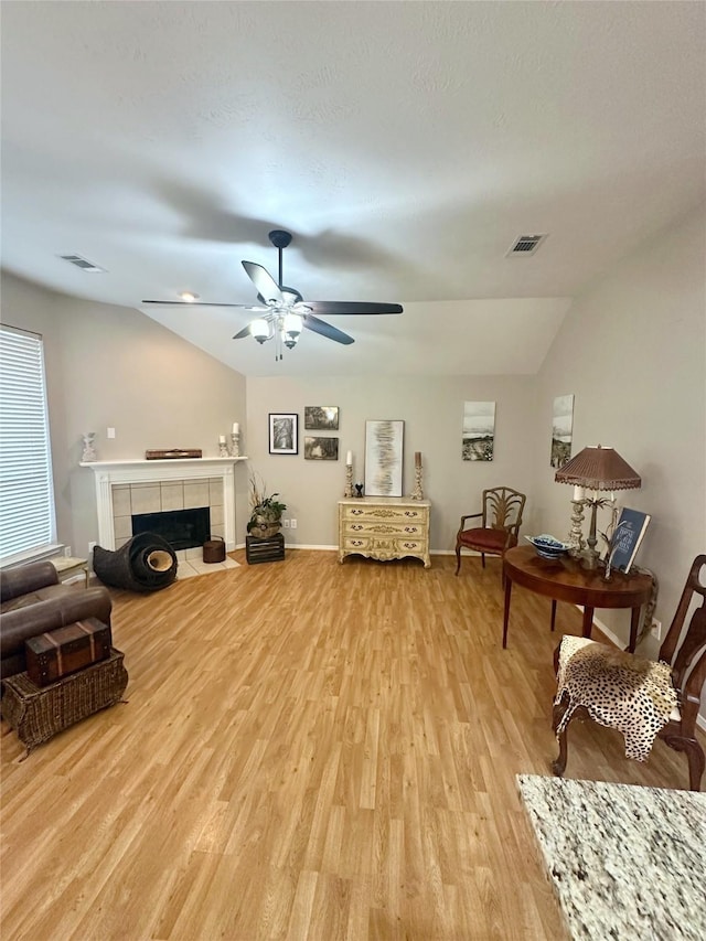 living room featuring a tile fireplace, ceiling fan, vaulted ceiling, and light wood-type flooring