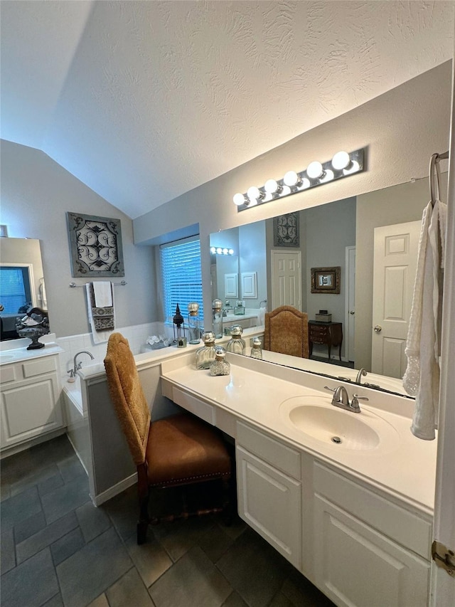 bathroom featuring a textured ceiling, a bathing tub, vanity, and lofted ceiling