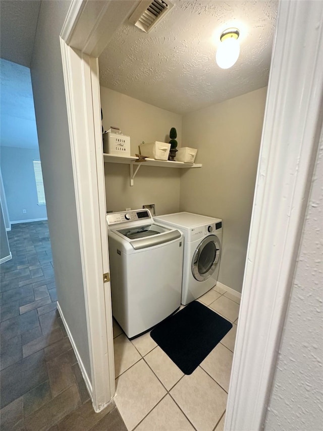 clothes washing area with a textured ceiling, washer and clothes dryer, and light tile patterned flooring