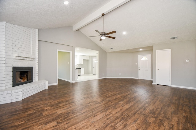 unfurnished living room with a brick fireplace, ceiling fan, a textured ceiling, beam ceiling, and dark hardwood / wood-style flooring