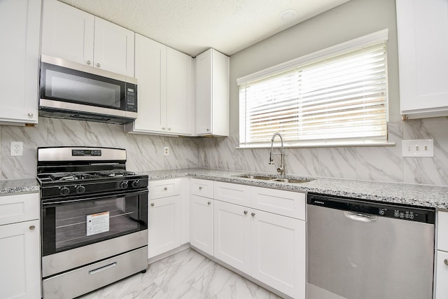 kitchen with white cabinets, sink, light stone countertops, a textured ceiling, and stainless steel appliances