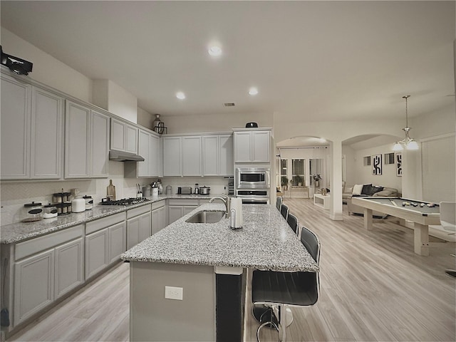 kitchen with sink, stainless steel appliances, light hardwood / wood-style flooring, pendant lighting, and a kitchen island with sink