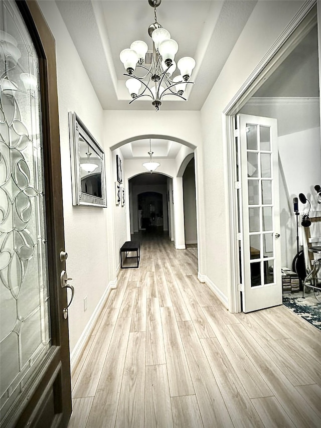 corridor featuring an inviting chandelier, light wood-type flooring, french doors, and a tray ceiling