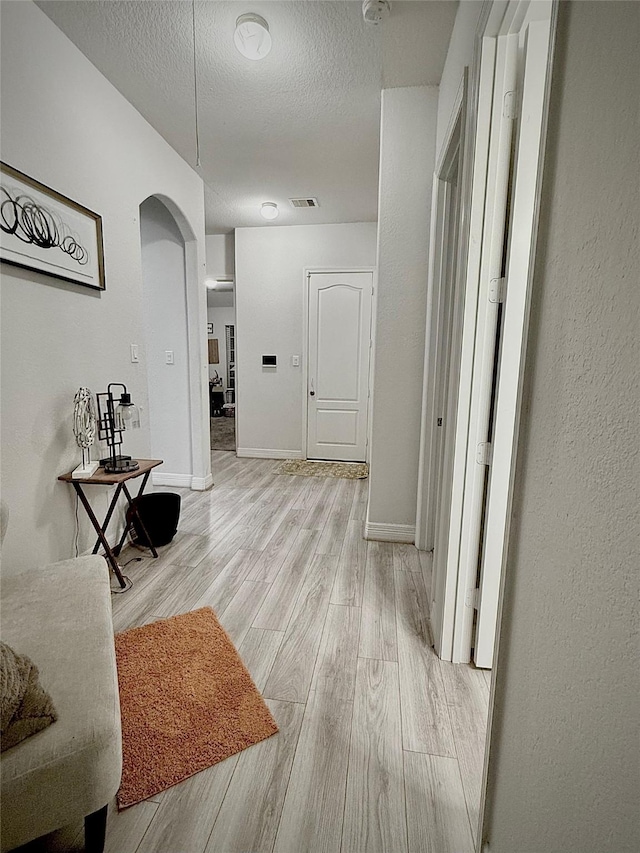 corridor with light wood-type flooring and a textured ceiling