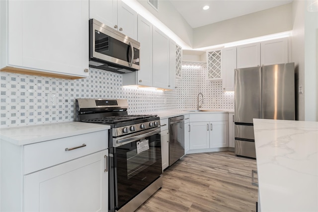 kitchen with decorative backsplash, light stone countertops, stainless steel appliances, light hardwood / wood-style floors, and white cabinetry