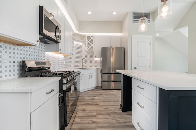 kitchen featuring appliances with stainless steel finishes, sink, decorative light fixtures, light hardwood / wood-style floors, and white cabinetry