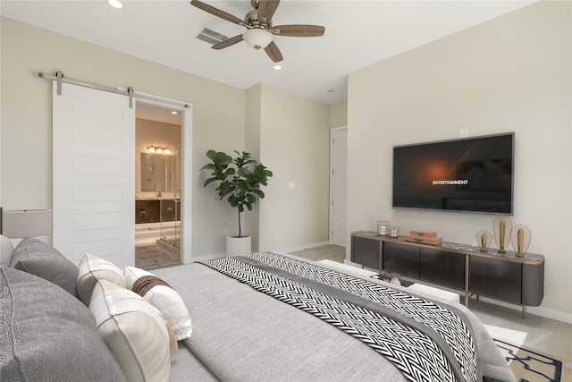 carpeted bedroom with ensuite bathroom, a barn door, and ceiling fan