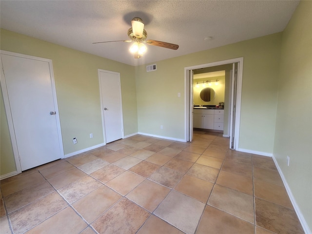 unfurnished bedroom featuring ceiling fan, connected bathroom, light tile patterned floors, and a textured ceiling