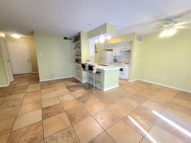 kitchen with kitchen peninsula, a breakfast bar area, ceiling fan, white appliances, and white cabinets