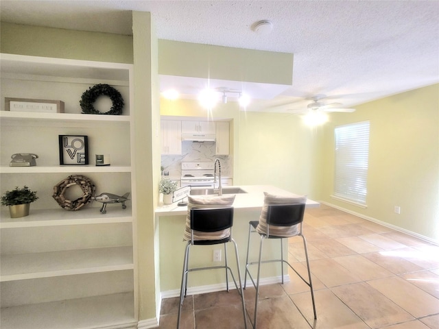 kitchen featuring ceiling fan, a breakfast bar, electric range, sink, and a textured ceiling