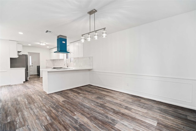 kitchen featuring backsplash, kitchen peninsula, wall chimney exhaust hood, dark hardwood / wood-style flooring, and white cabinetry