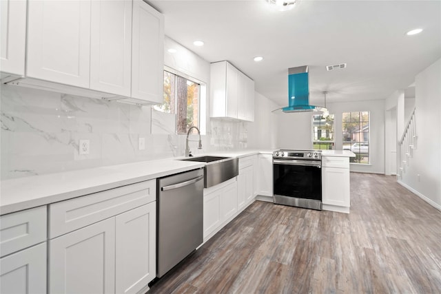 kitchen featuring appliances with stainless steel finishes, island range hood, white cabinetry, and plenty of natural light