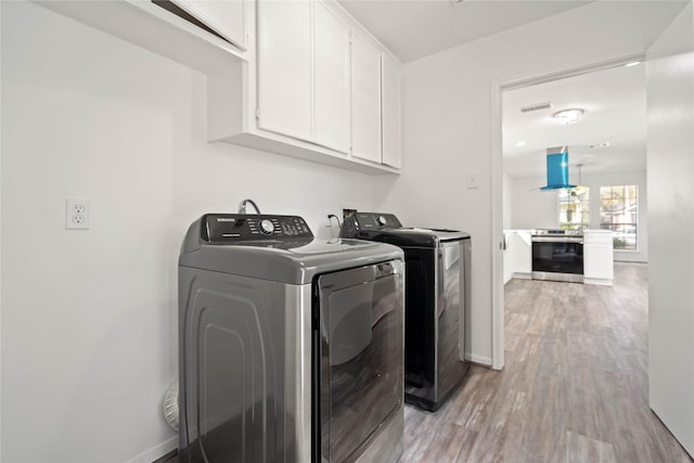 clothes washing area featuring washer and dryer, cabinets, and light wood-type flooring