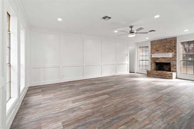 unfurnished living room with ceiling fan, wood-type flooring, ornamental molding, and a brick fireplace