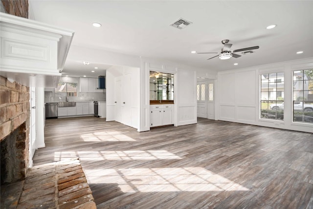 unfurnished living room with ceiling fan, sink, a stone fireplace, hardwood / wood-style floors, and ornamental molding