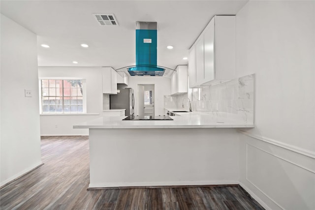 kitchen with stainless steel refrigerator, kitchen peninsula, island range hood, and white cabinets