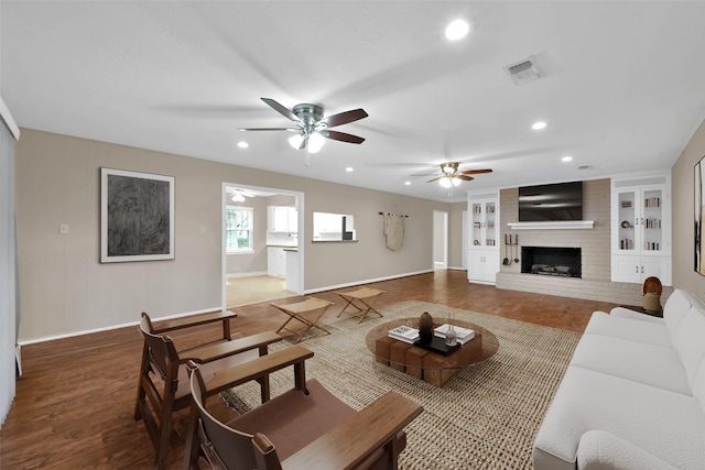 living room featuring built in shelves, ceiling fan, a fireplace, and hardwood / wood-style flooring