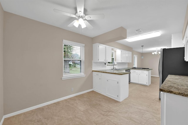 kitchen with kitchen peninsula, ceiling fan with notable chandelier, sink, dark stone countertops, and white cabinetry