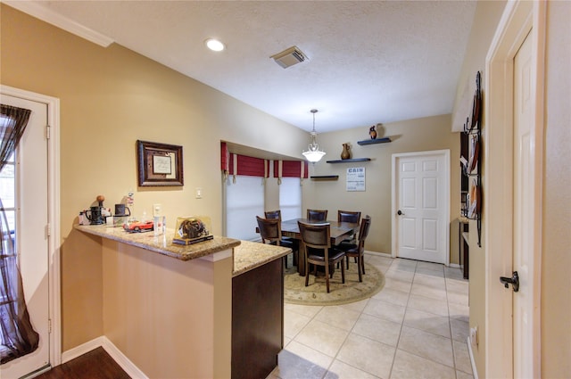 kitchen with hanging light fixtures, light stone countertops, a textured ceiling, light tile patterned flooring, and kitchen peninsula