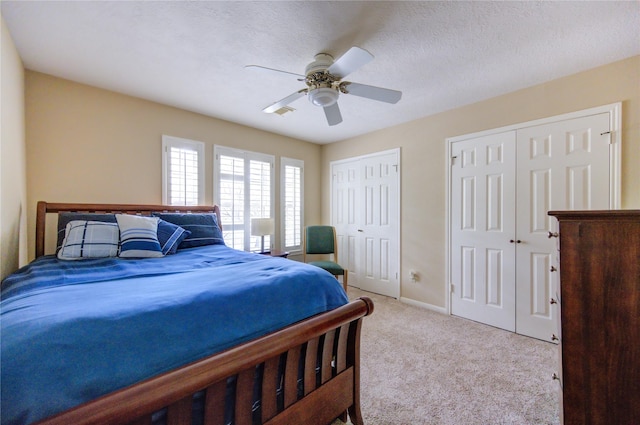 bedroom featuring ceiling fan, a textured ceiling, light carpet, and multiple closets