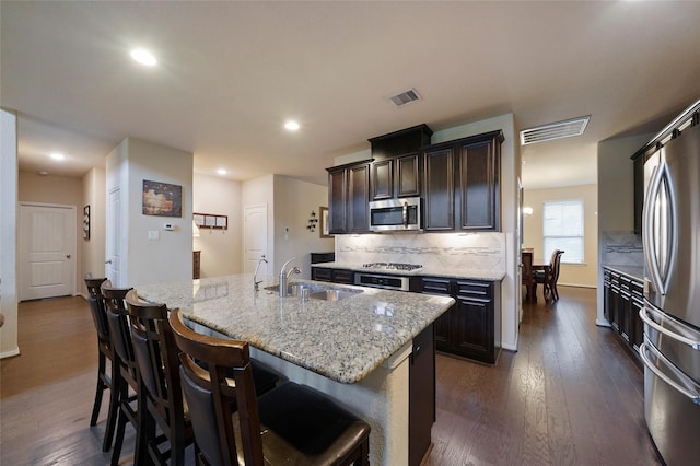 kitchen with dark hardwood / wood-style flooring, a breakfast bar, stainless steel appliances, sink, and a center island with sink