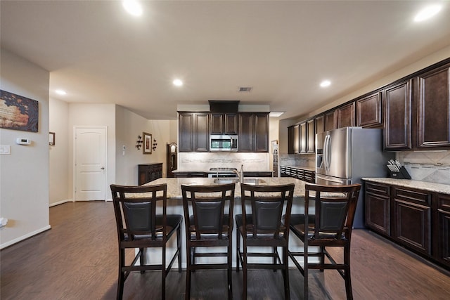 kitchen featuring decorative backsplash, dark hardwood / wood-style floors, an island with sink, appliances with stainless steel finishes, and dark brown cabinetry