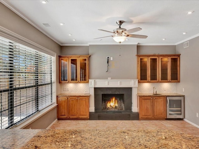 unfurnished living room featuring ornamental molding, ceiling fan, sink, a premium fireplace, and wine cooler